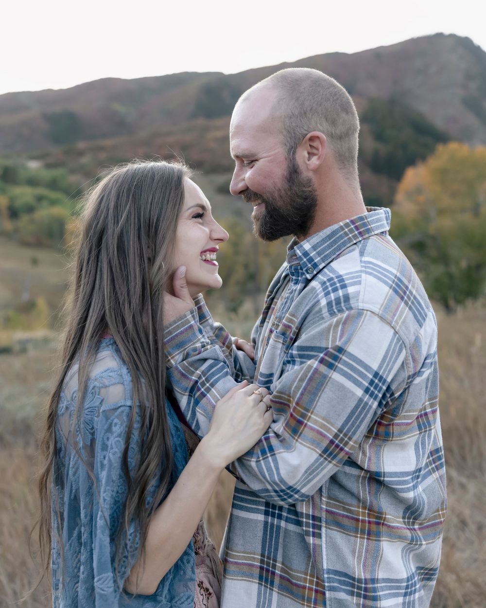 A couple shares a romantic moment together in a natural outdoor setting wearing coordinated plaid and denim outfits.
