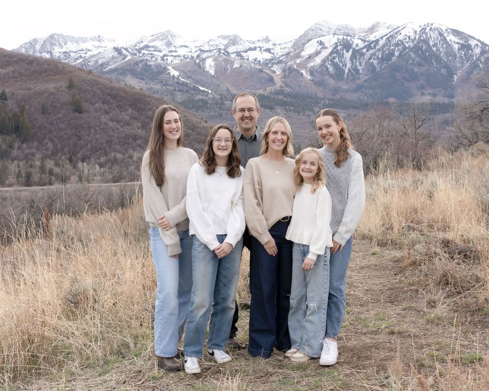 A group poses together on a hiking trail with snow-capped mountains in the background during fall.