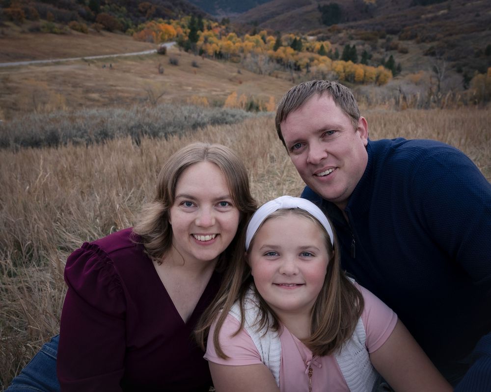 Group of people posing together outdoors against scenic mountain backdrop with autumn foliage in background.