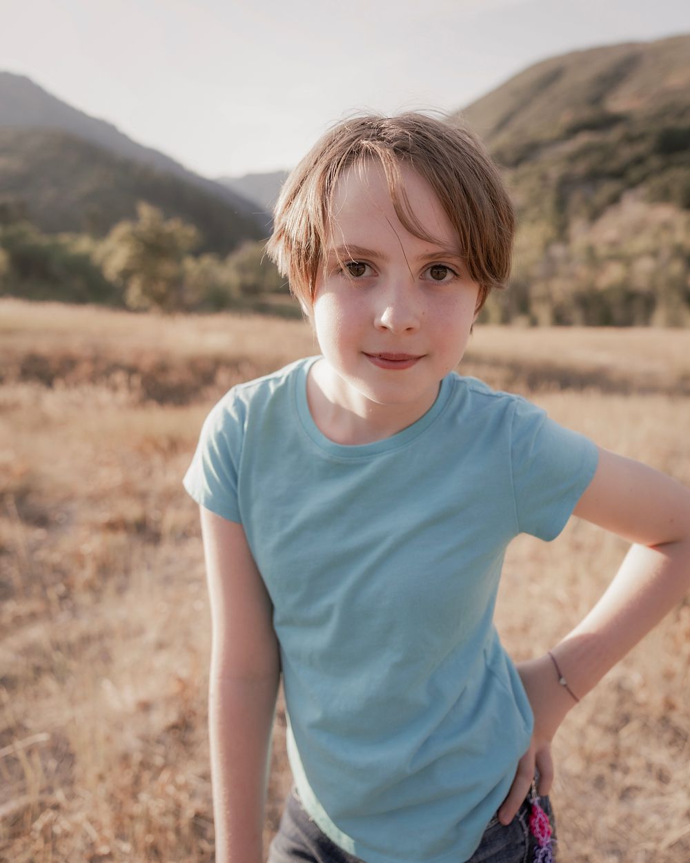 Active poses in a light blue t-shirt against a mountain landscape.