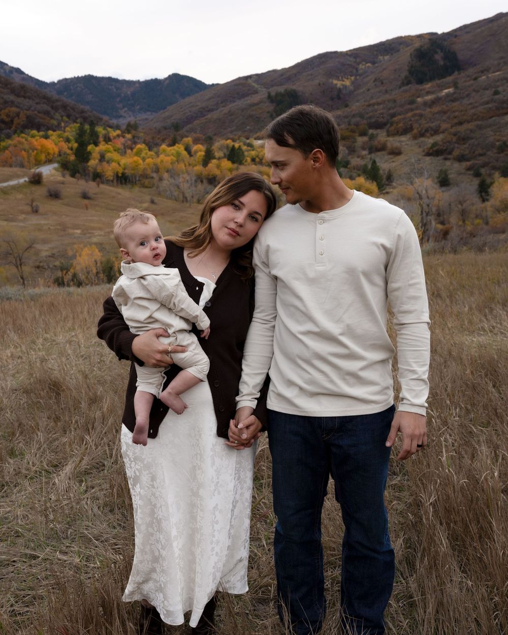 Family in coordinating cream and black outfits poses together in a rustic mountain field during autumn.