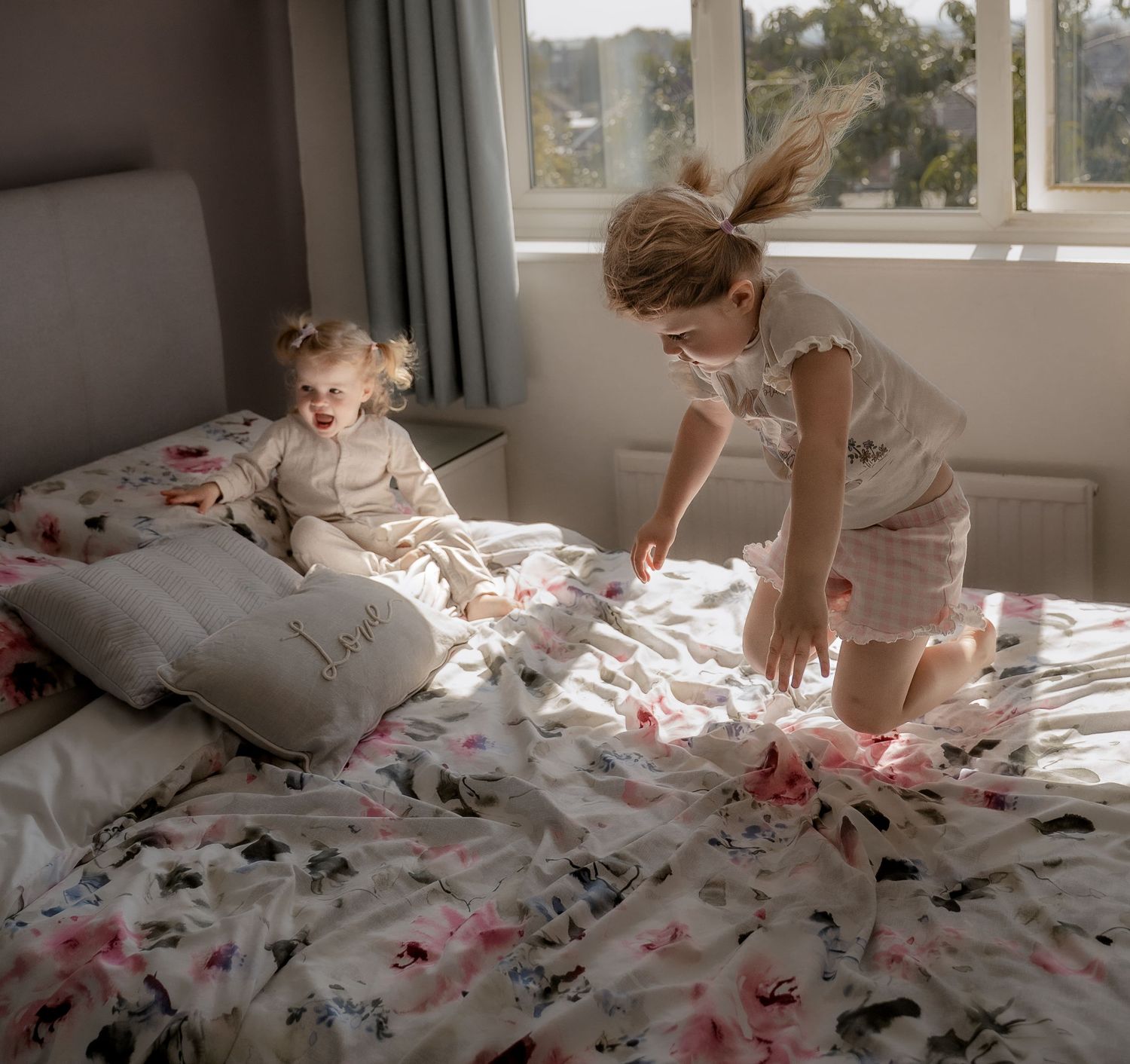 Sisters laughing and playing together on the bed during a natural lifestyle family photography session in Derbyshire.