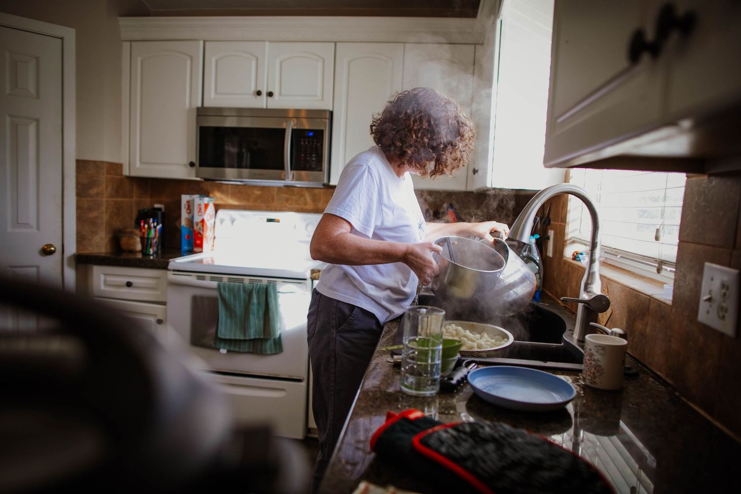 Senior woman in a bright kitchen arranges fresh ingredients while preparing a meal at home.