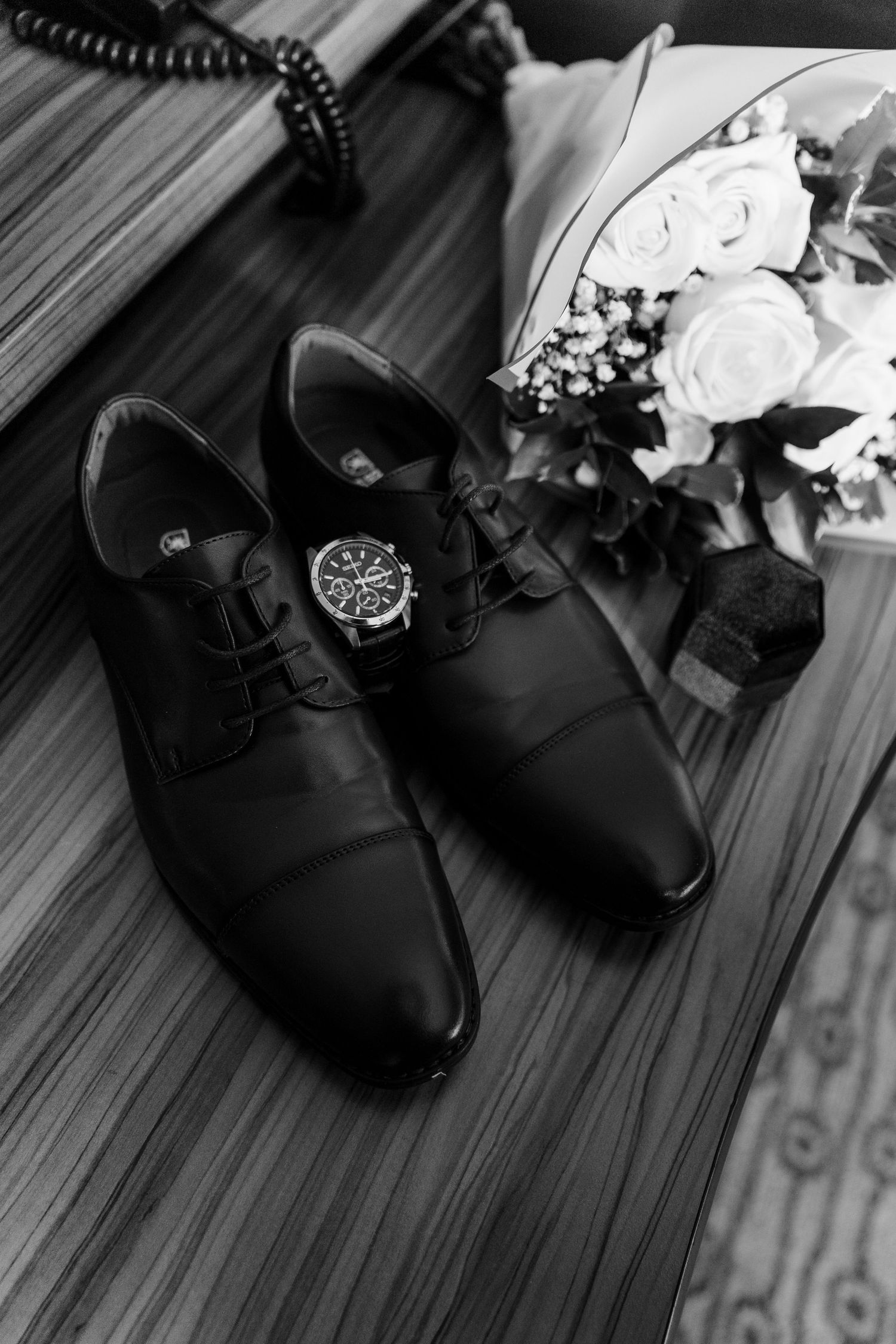 Black leather dress shoes arranged on a hardwood floor in a diagonal line reflecting a formal style.