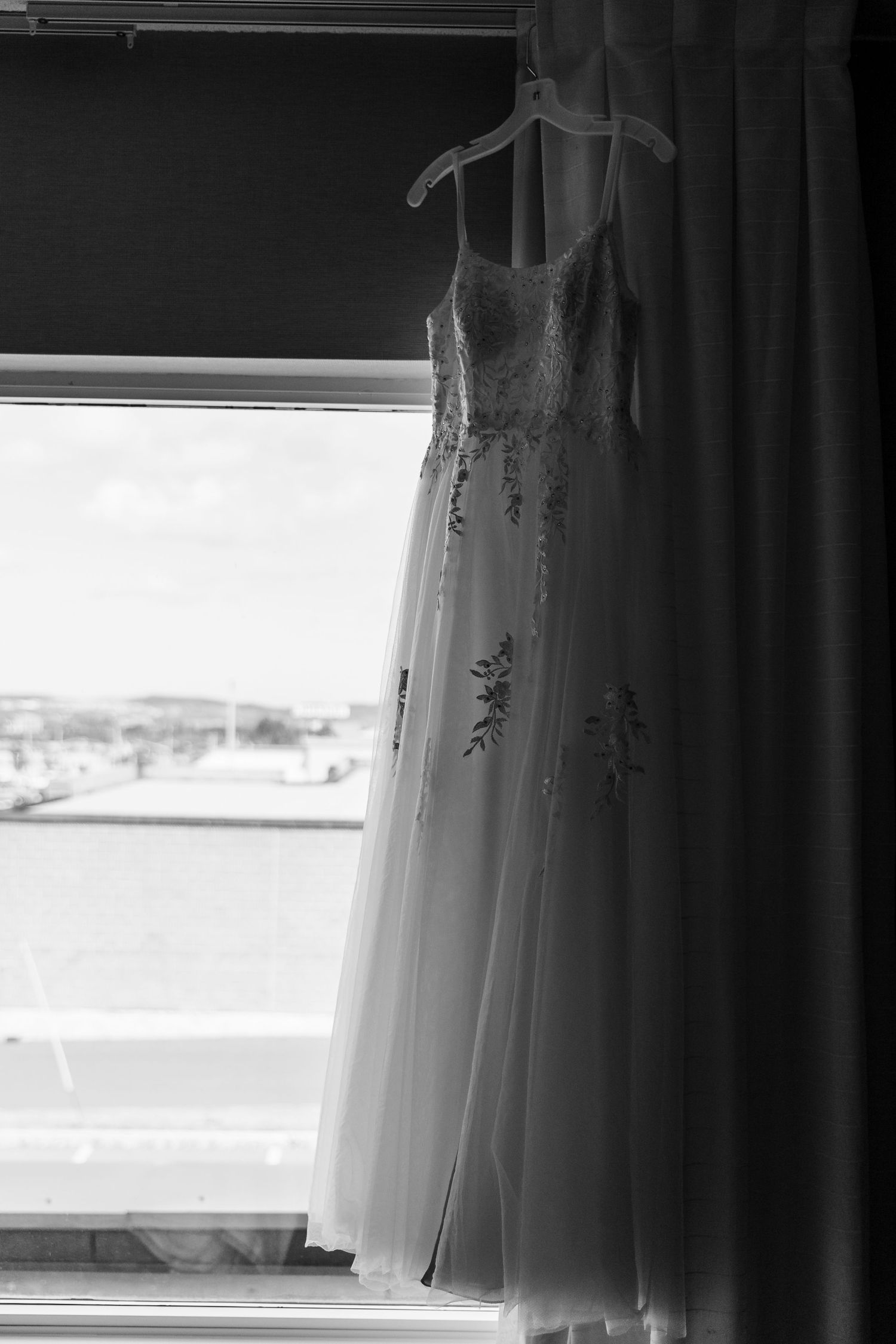 A dramatic black and white view through an opened window with white curtains framing a sunny outdoor landscape.