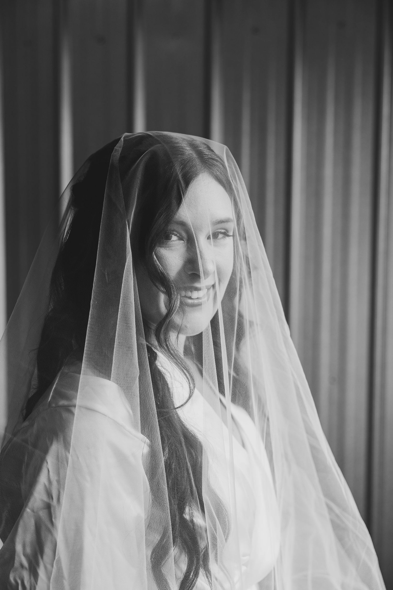 A black and white wedding portrait shows a bride in a delicate veil smiling softly at the camera.