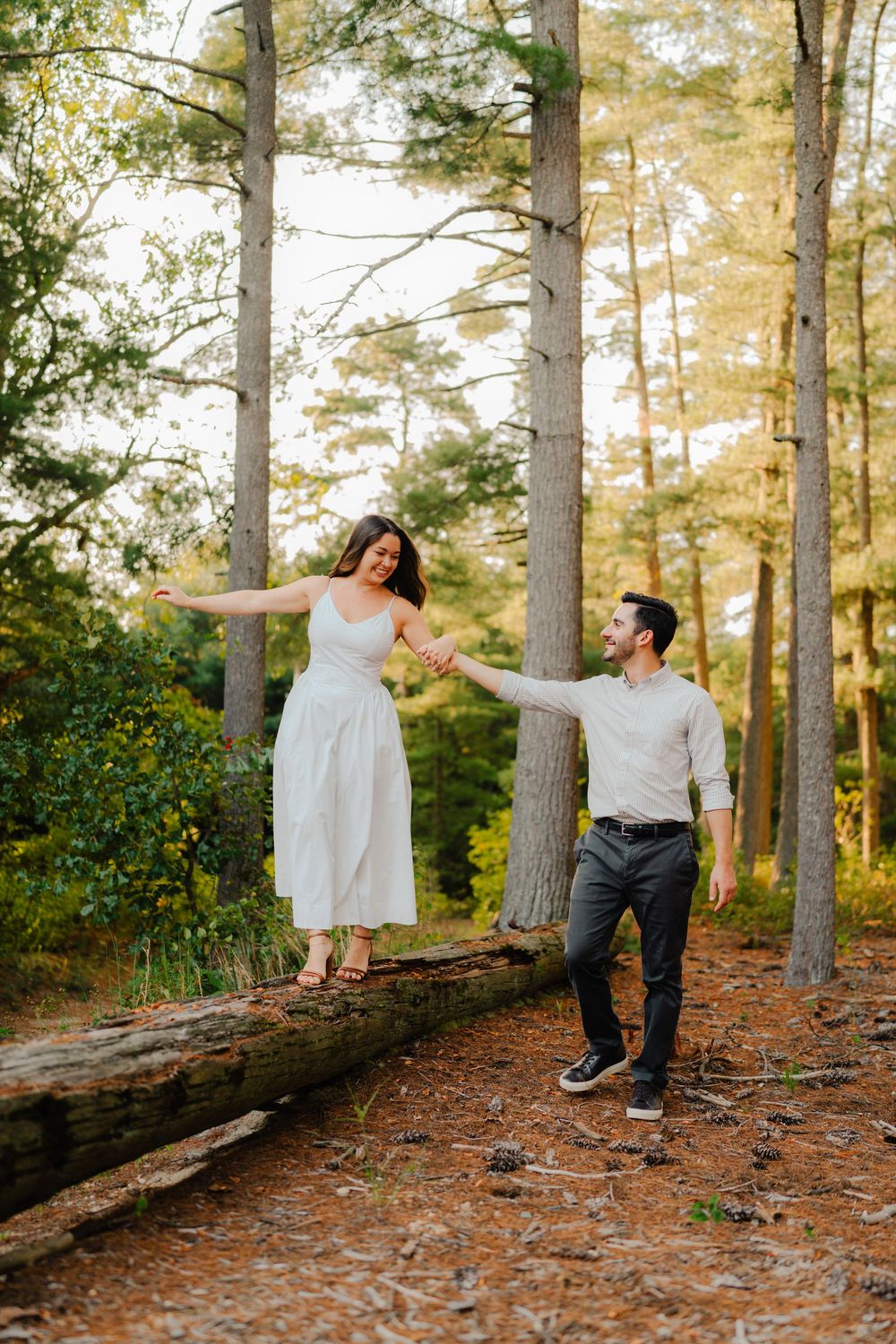 Two people balance playfully on a fallen log in a pine forest during a photo session.