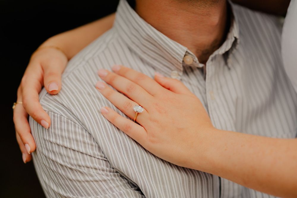 Close-up shot of hands wearing rings resting on a striped button-down shirt in soft lighting.