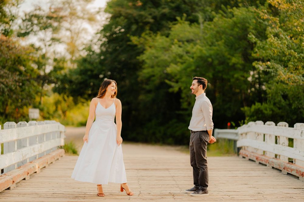 Two figures walking along a rustic wooden bridge surrounded by lush greenery during a sunset photoshoot.
