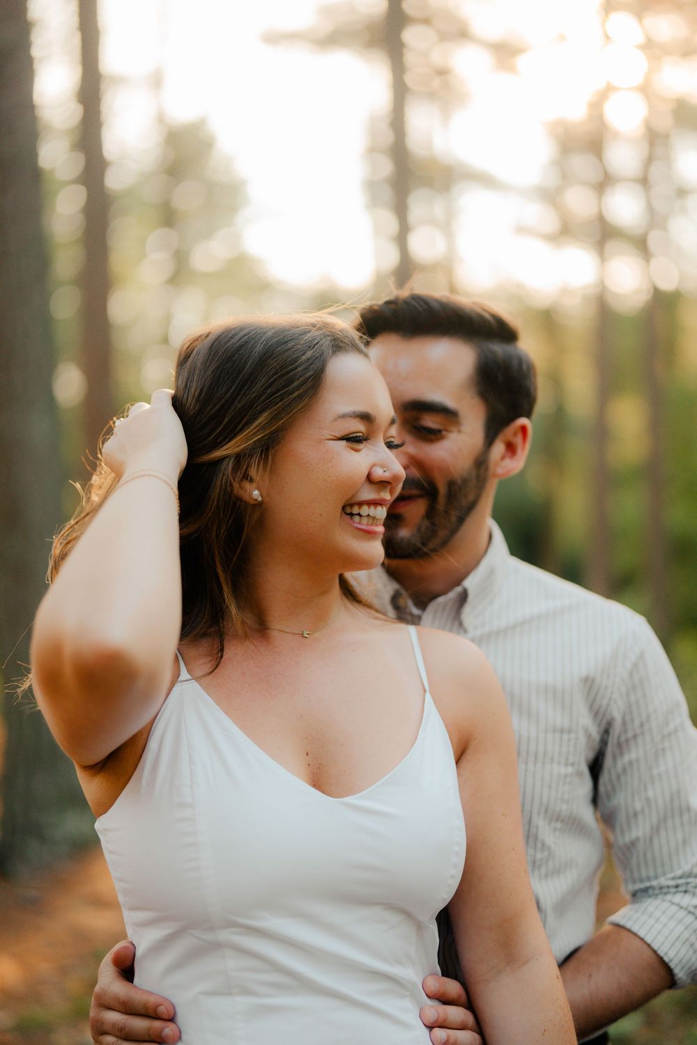 A romantic couple embraces in a forest setting during golden hour while wearing white and striped clothing.