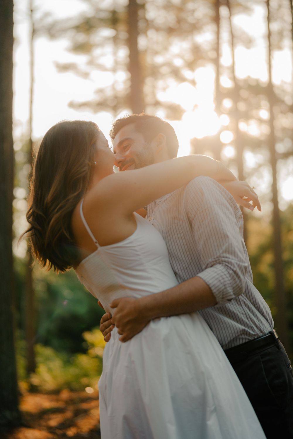 A tender moment captured between two people embracing in a sunlit forest setting.