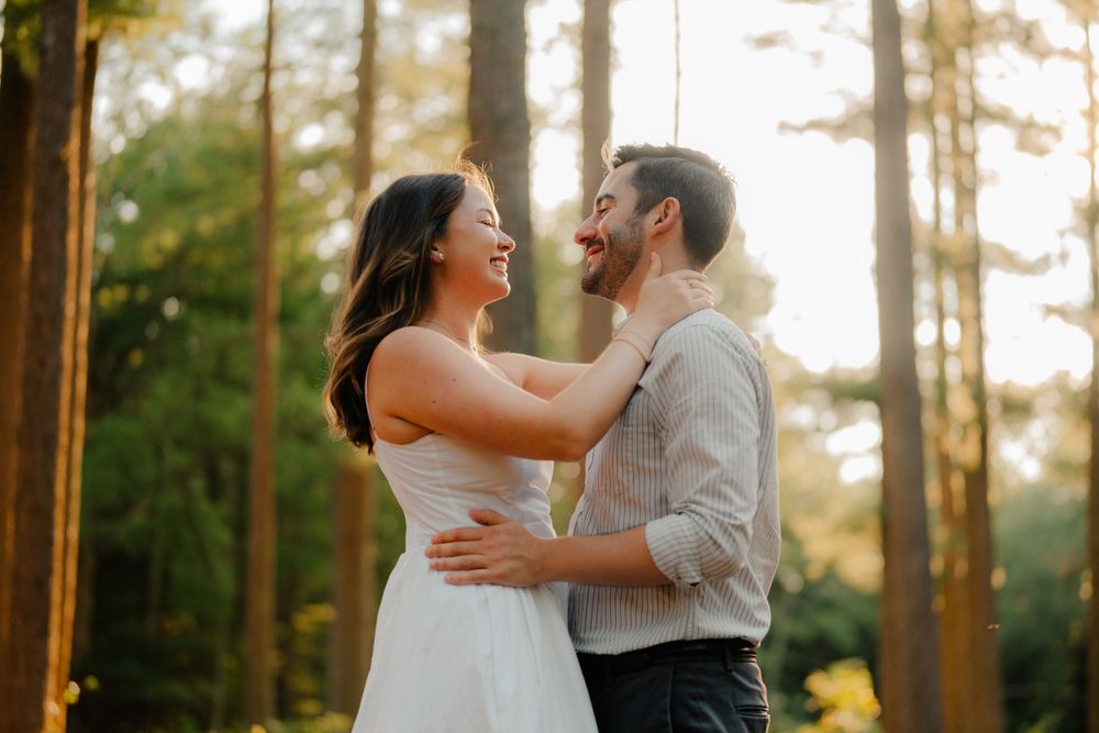 A couple in wedding attire share a joyful moment during an outdoor photo session in a tranquil pine forest.