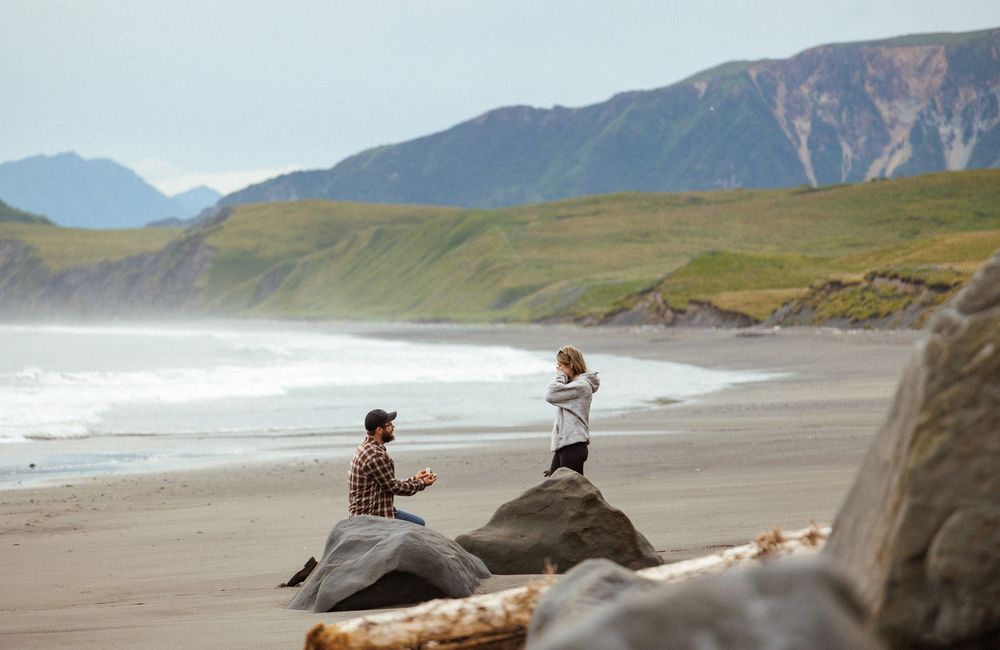 Rocky coastline with dramatic mountains and dark sand beach stretching into the distance.