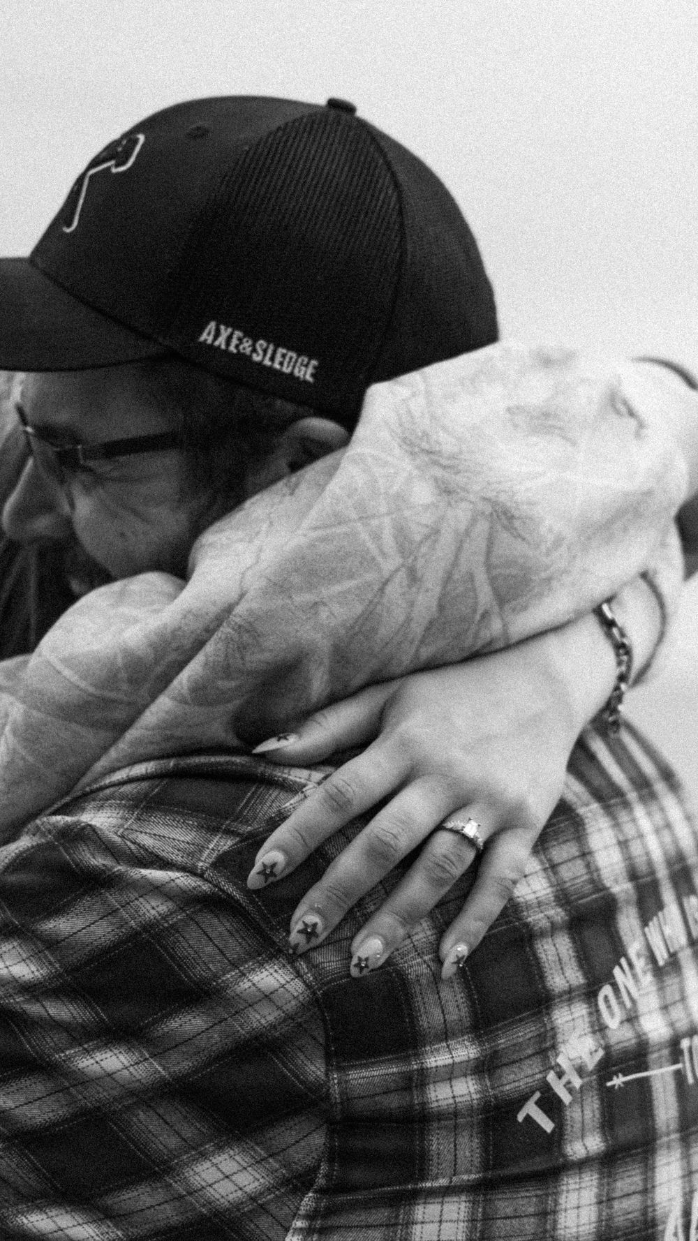 Black and white photo showing a close embrace with tattooed arms and a baseball cap.