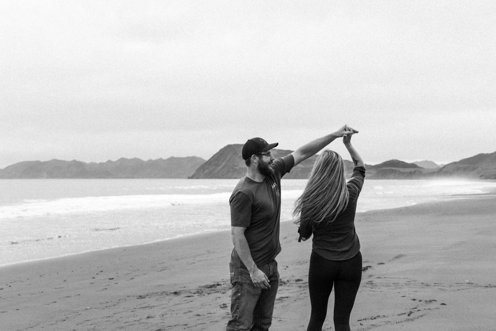 Couple enjoying a moment together on a scenic black sand beach with mountains in background.