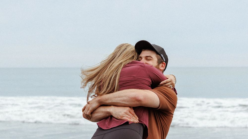 Couple embracing on a beach with waves in the background on an overcast day.