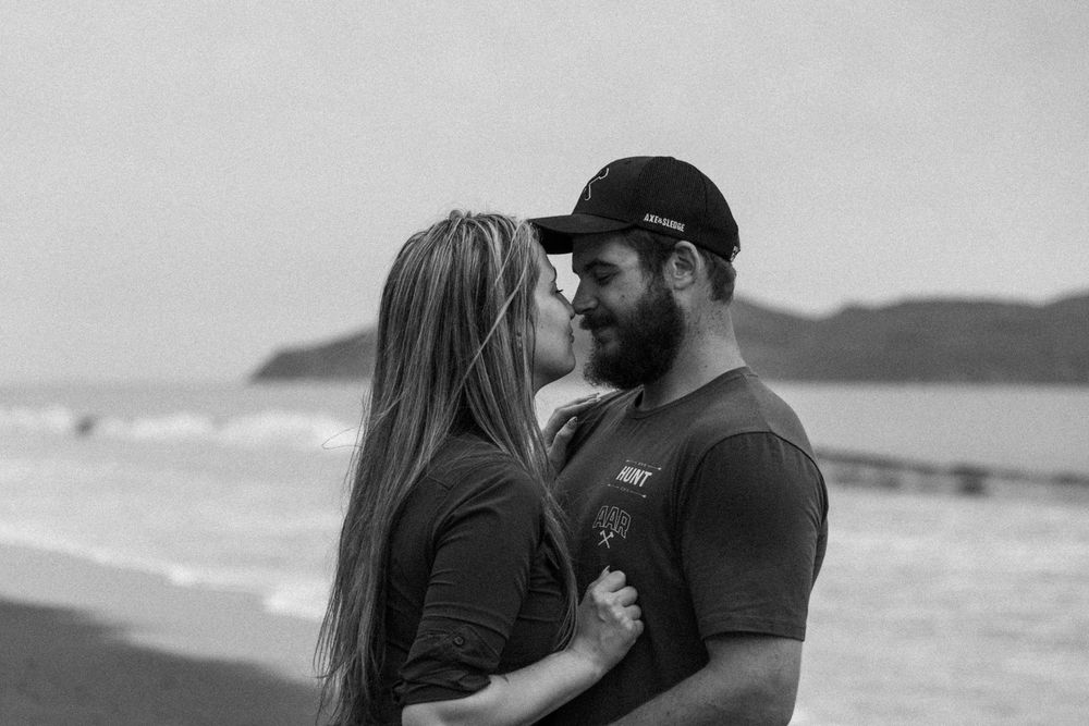Romantic beach photoshoot featuring two people in casual attire against coastal backdrop.