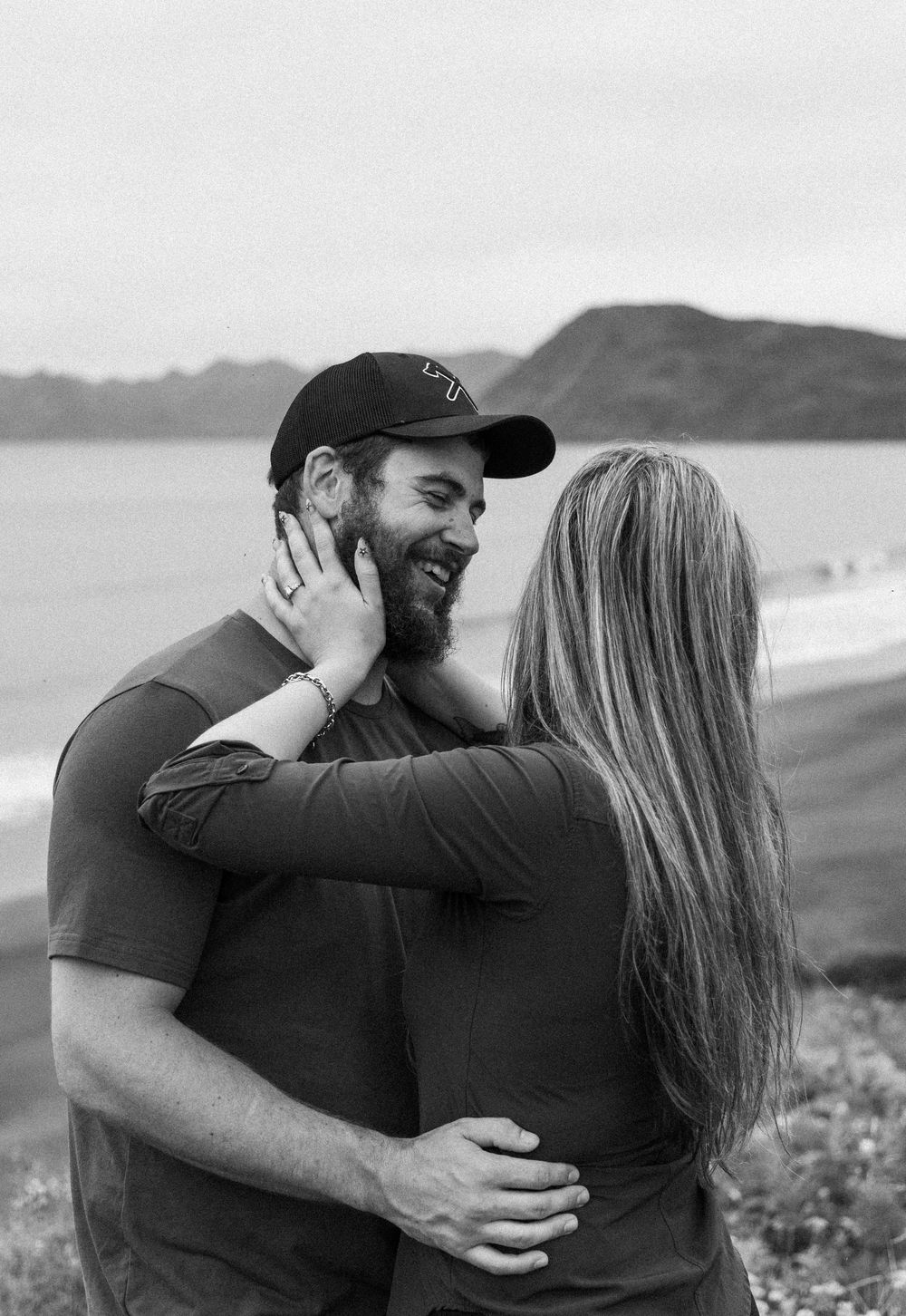 Intimate black and white photos of a couple sharing tender moments on a coastal overlook.