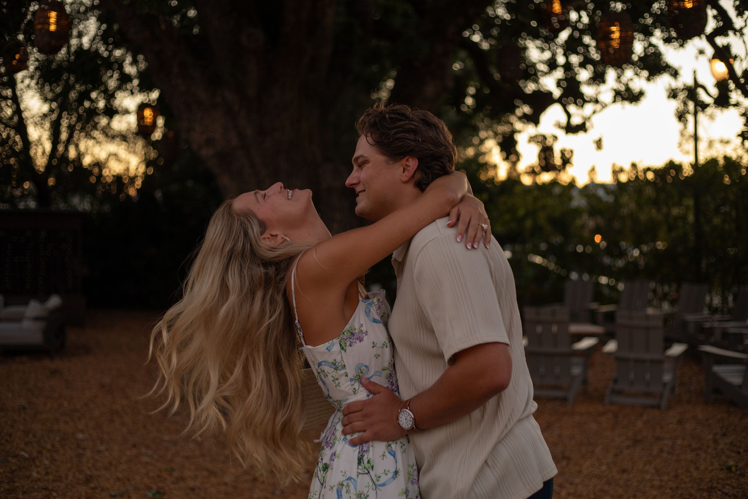 Romantic couple embraces in a dreamy outdoor setting during golden hour with trees in the background.