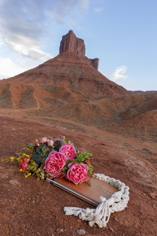 Desert mesa landscape with pink roses and white lace arranged on red rocks against towering sandstone buttes.