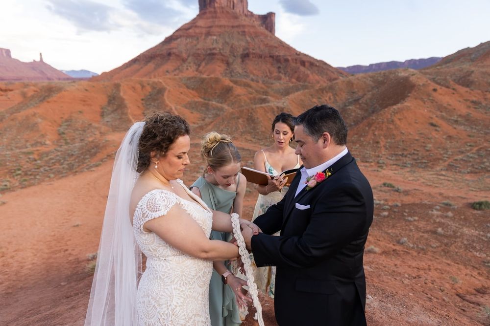 A couple shares a romantic moment together in a scenic canyon landscape with red sandstone cliffs and blue skies in Utah.
