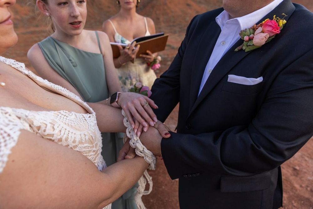 A couple exchanges rings during an outdoor wedding ceremony with red rock formations in the background.