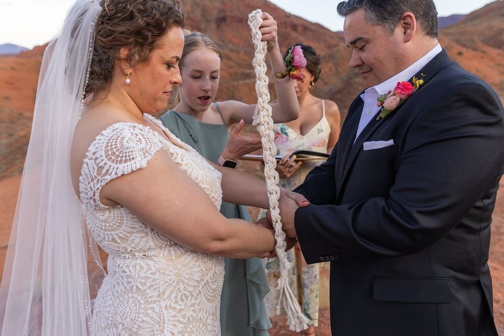 A wedding ceremony takes place in front of stunning red rock formations in a desert landscape.
