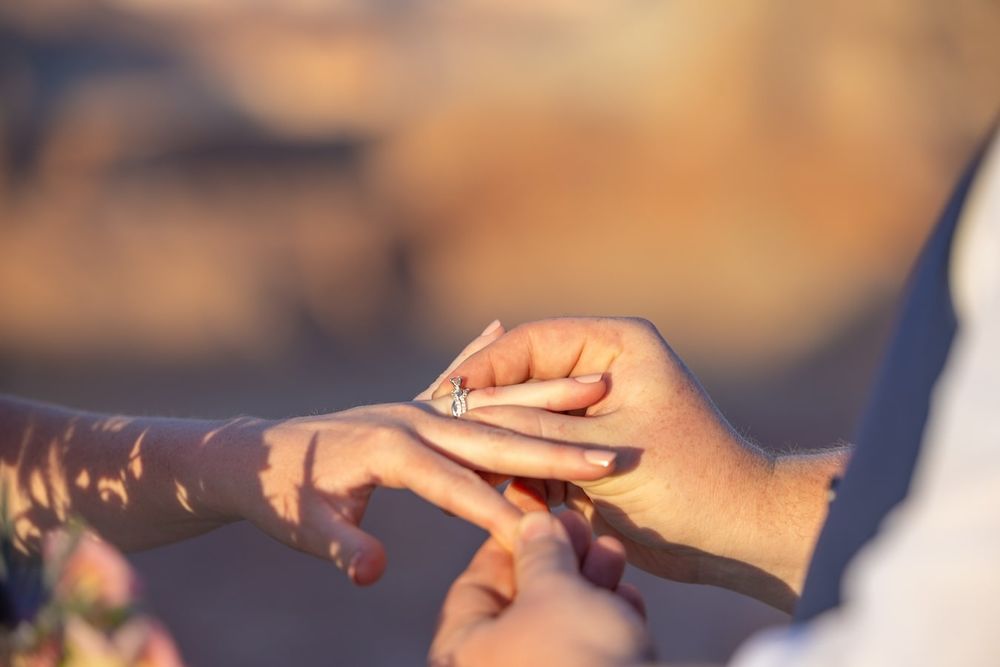 Close up photo of hands exchanging a white gift box with red bow against blurred warm background.