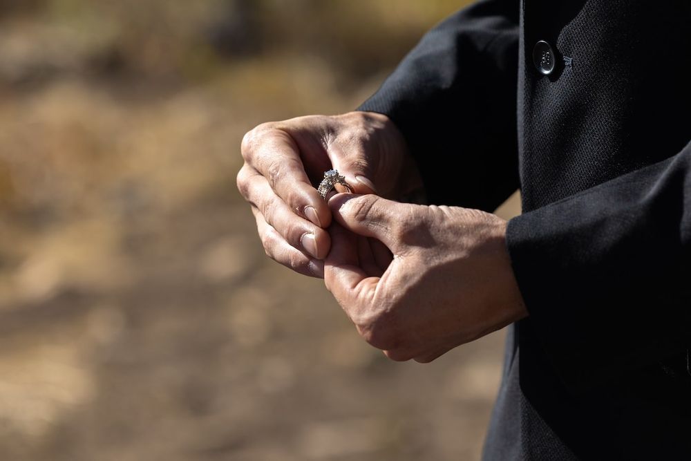 Close-up shot of hands clasped together wearing a dark sweater against a blurred natural outdoor background.