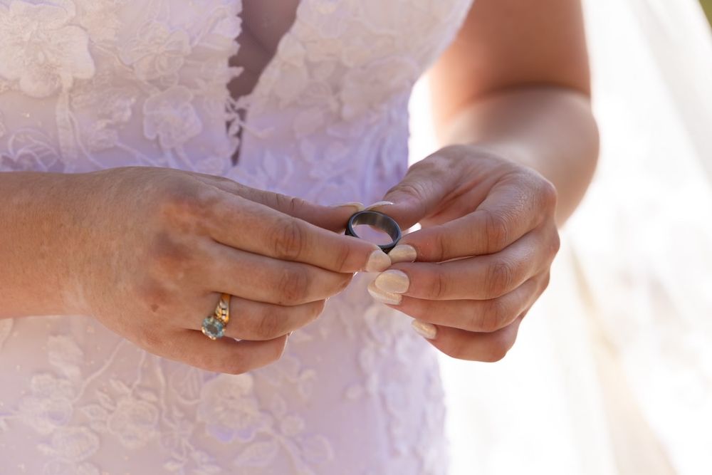 Close-up sequence of hands placing a diamond engagement ring on a finger with delicate lace in the background.