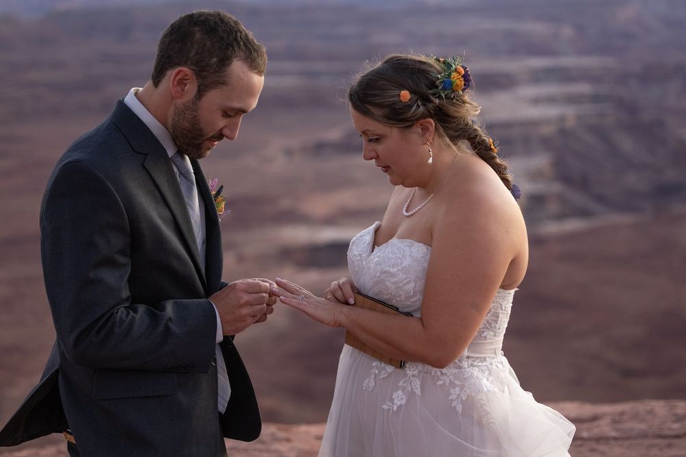 A couple in wedding attire shares an intimate moment against a scenic desert canyon backdrop at sunset.