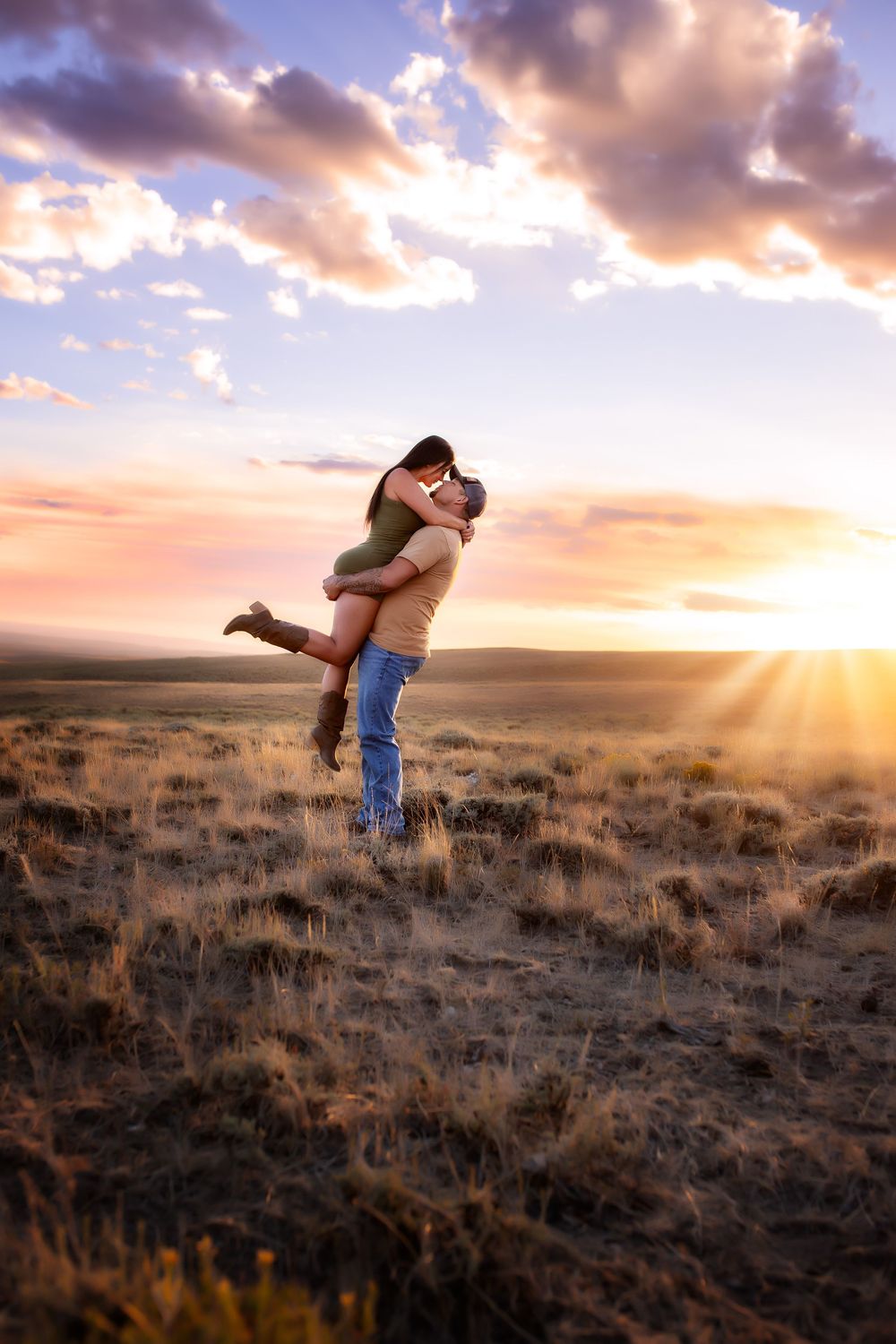 A couple embraces and spins joyfully in a desert field during a dramatic golden sunset.