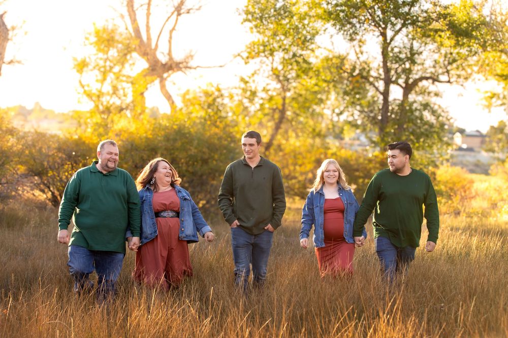 Group of people walking together through golden autumn field at sunset with glowing warm light and trees in background.