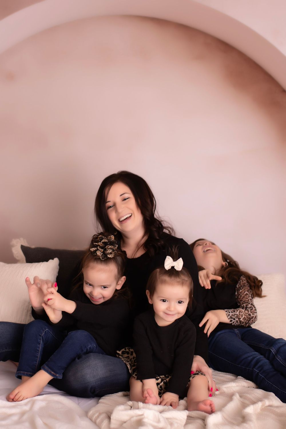 A joyful black and white photograph series showing playful moments between a parent and child on white bedding.