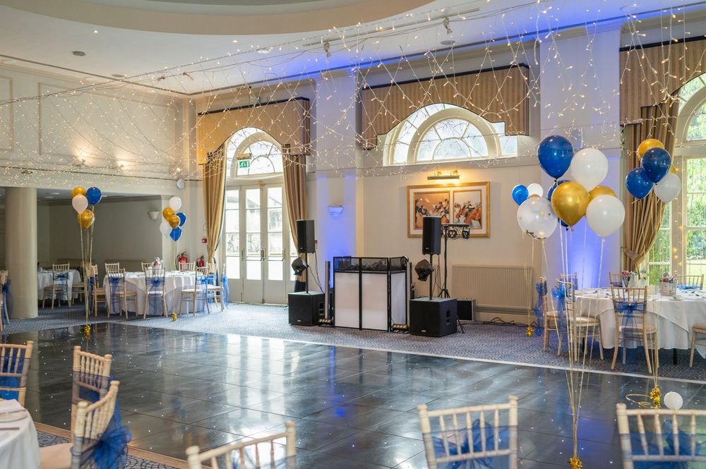 Elegant ballroom venue with arched windows, white chairs, and blue uplighting creating a romantic atmosphere.