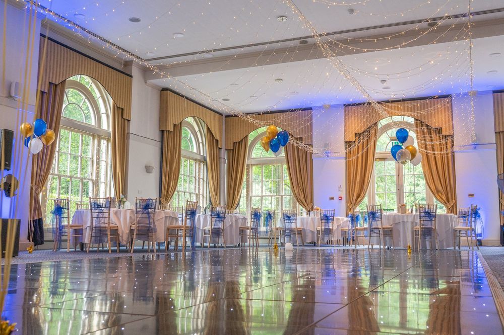 Grand ballroom with ornate crown molding, tall windows, and blue accent lighting for a formal event.