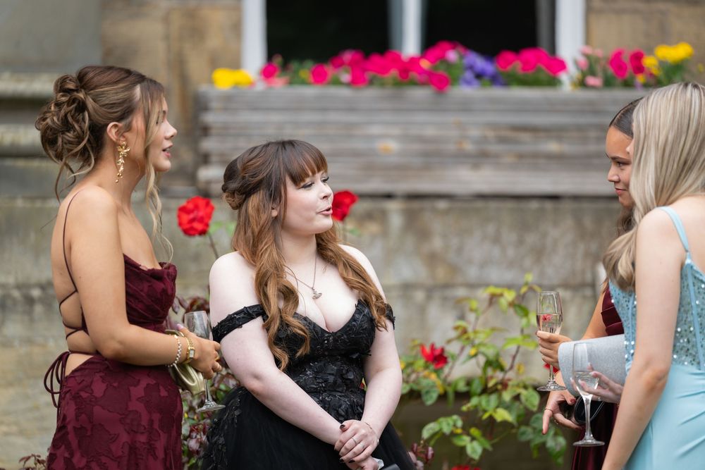 Guests in formal attire socializing outdoors near colorful flower gardens.