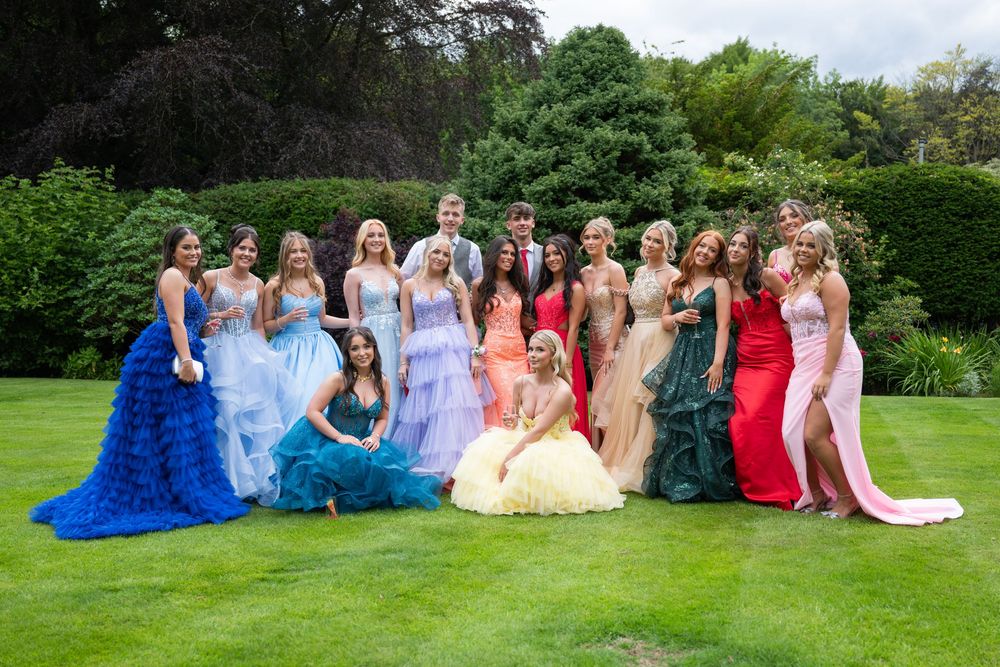 Large group in colorful formal attire posed on a lush green lawn for photos.