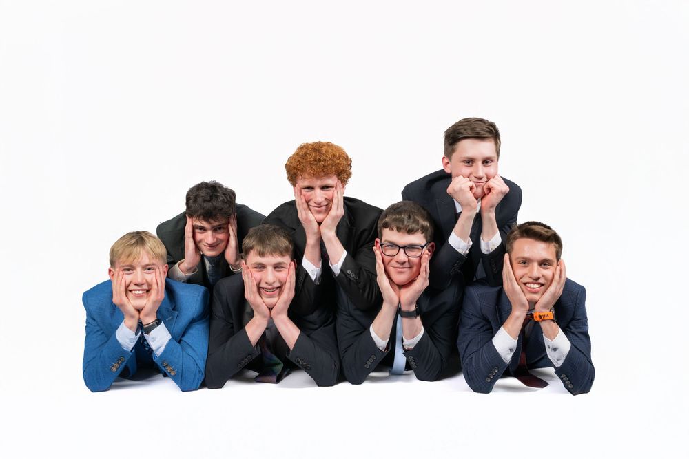 Group of young men in suits lying on floor in a row with hands on their faces posing for a fun portrait.
