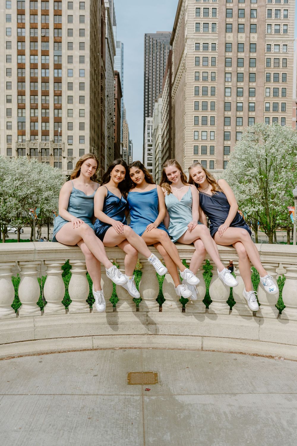 Five dancers in blue dresses and white sneakers sit together on a stone balustrade in downtown Chicago.