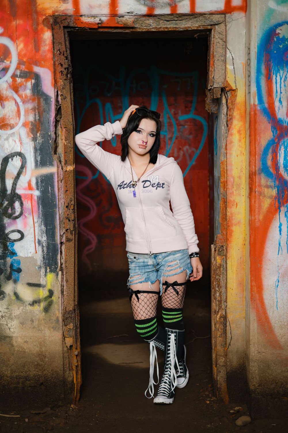 Street style fashion shoot with knee-high striped socks, converse sneakers and urban graffiti backdrop.