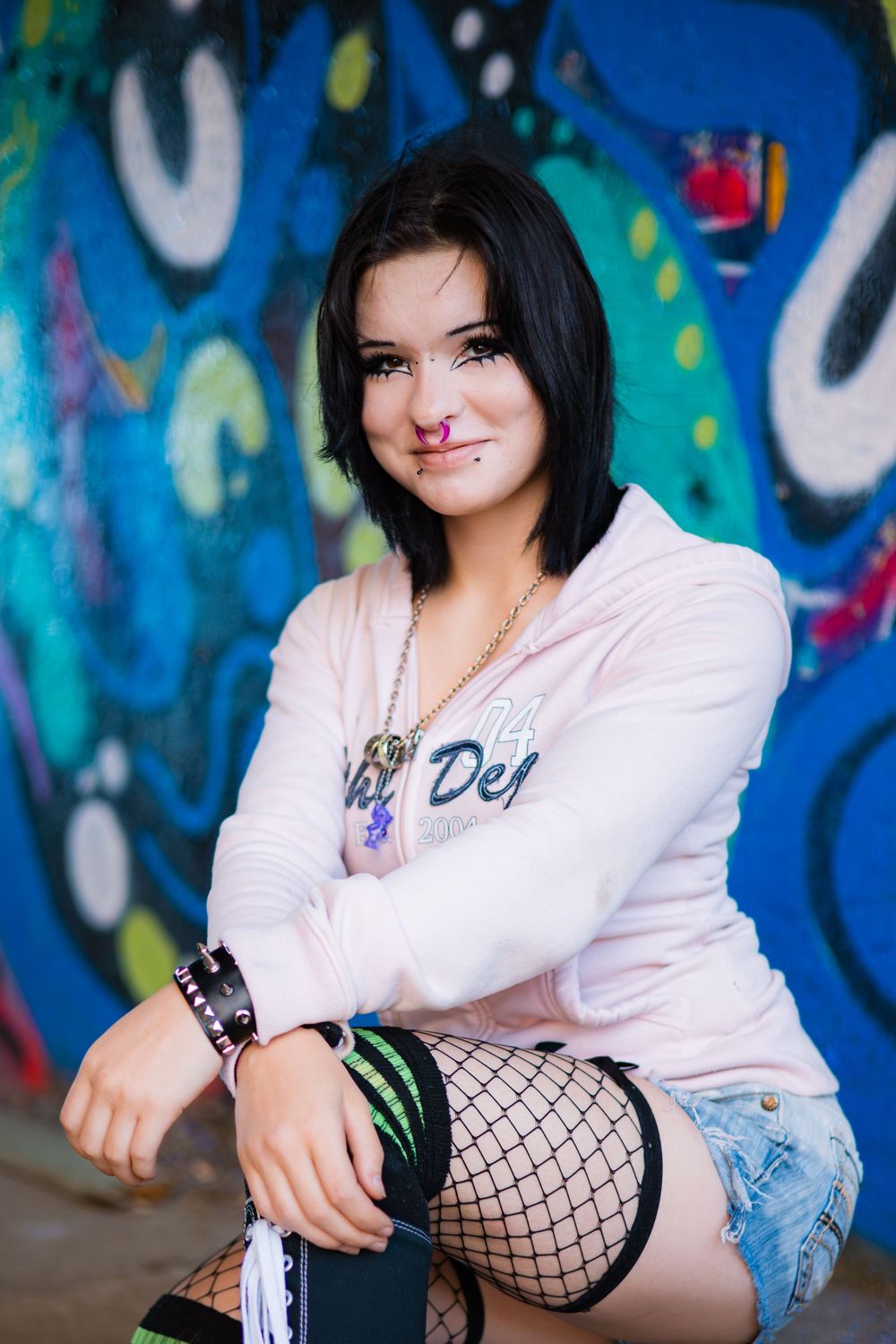 A fashion portrait against colorful graffiti wall showing edgy urban style with white jacket and fishnet stockings.