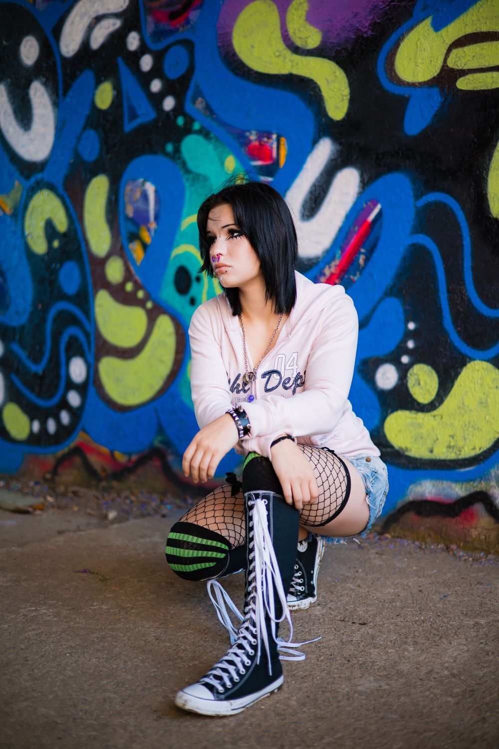 Casual portrait against vibrant blue graffiti wall with black sneakers and fishnet stockings.