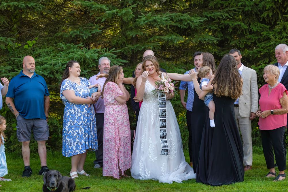 A group of wedding guests in summer attire stand together on a grassy lawn during an outdoor celebration.