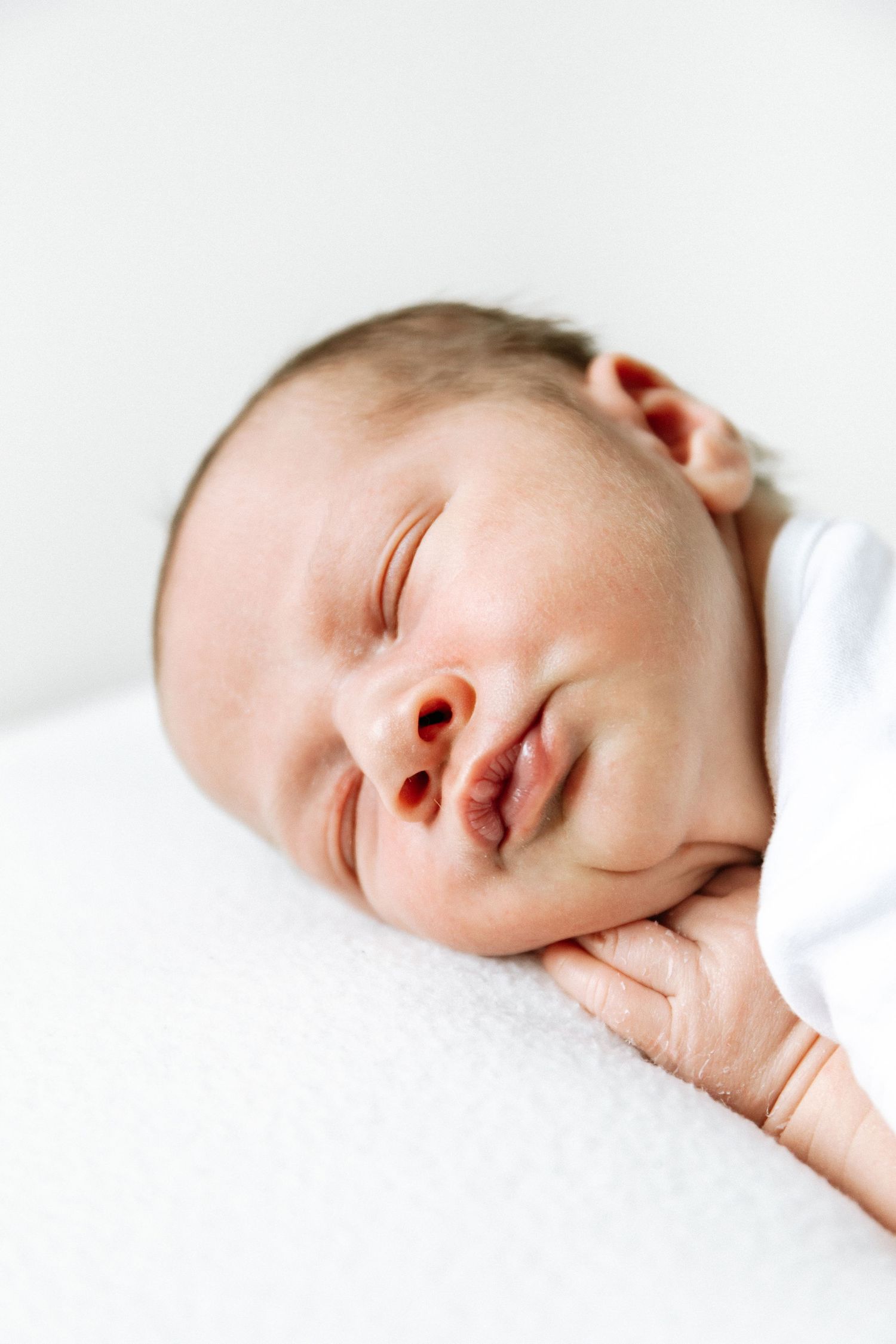 A sleeping newborn baby wrapped in soft white blankets rests peacefully against a white background during newborn shoot in Nottingham