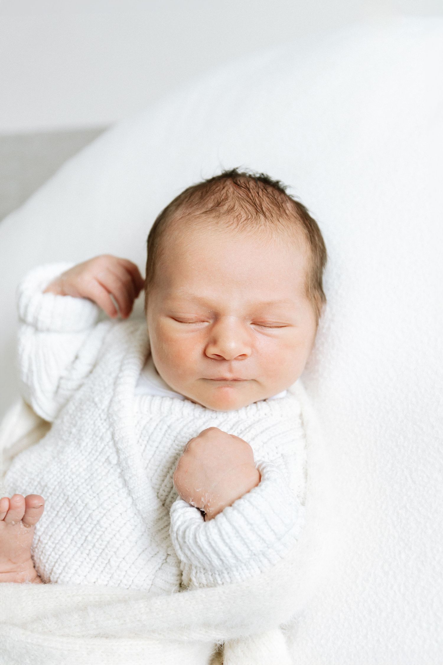 Peaceful sleeping newborn baby wrapped in soft white knitted blanket in natural light setting during newborn shoot in Nottingham