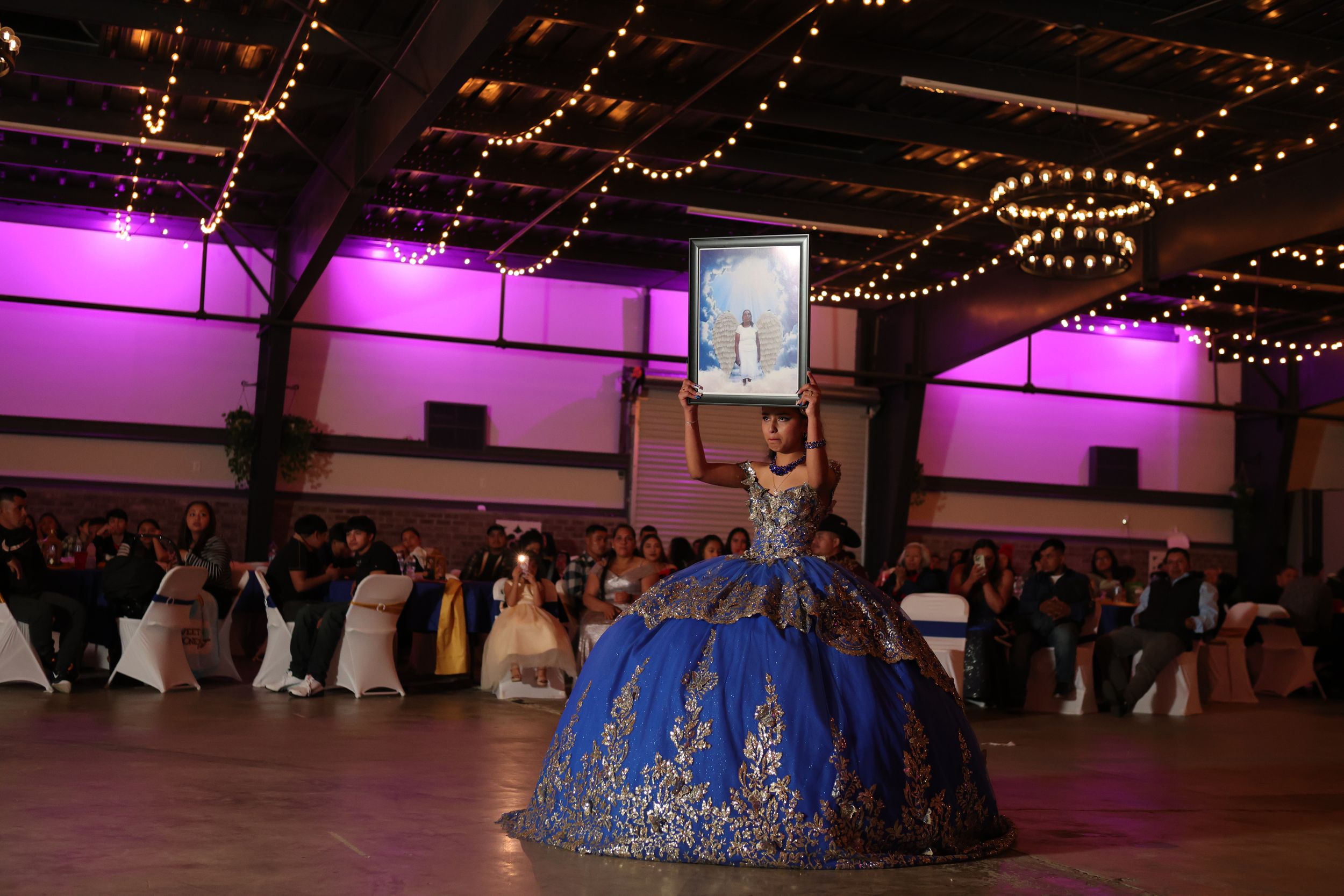People dancing at a reception venue decorated with twinkling string lights and purple accent lighting overhead.