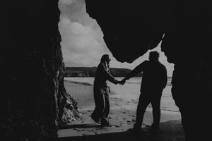 Romantic black and white silhouette of couple holding hands framed by coastal sea cave.