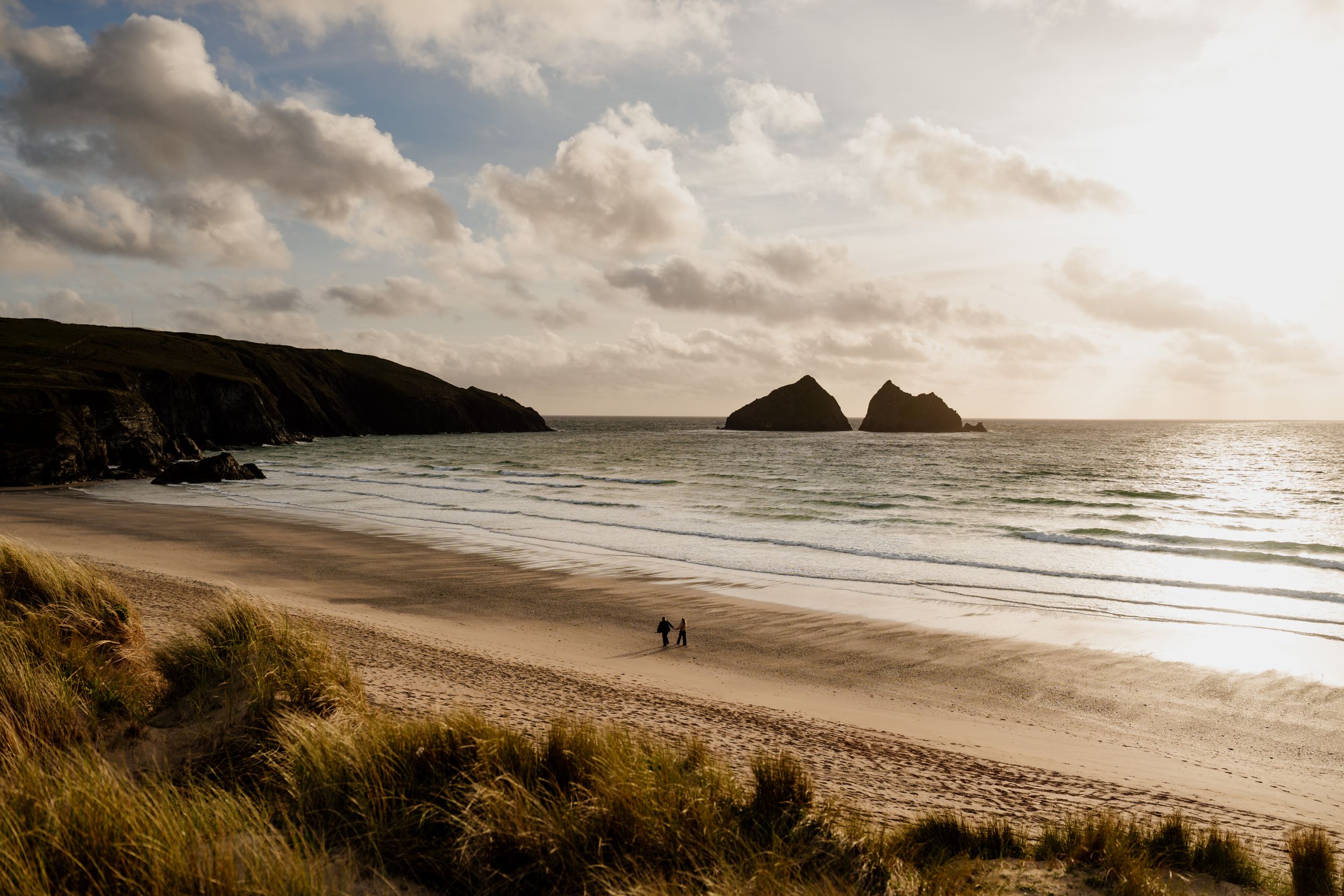 Golden hour sunset over a sweeping sandy beach with two small figures walking near the shoreline.
