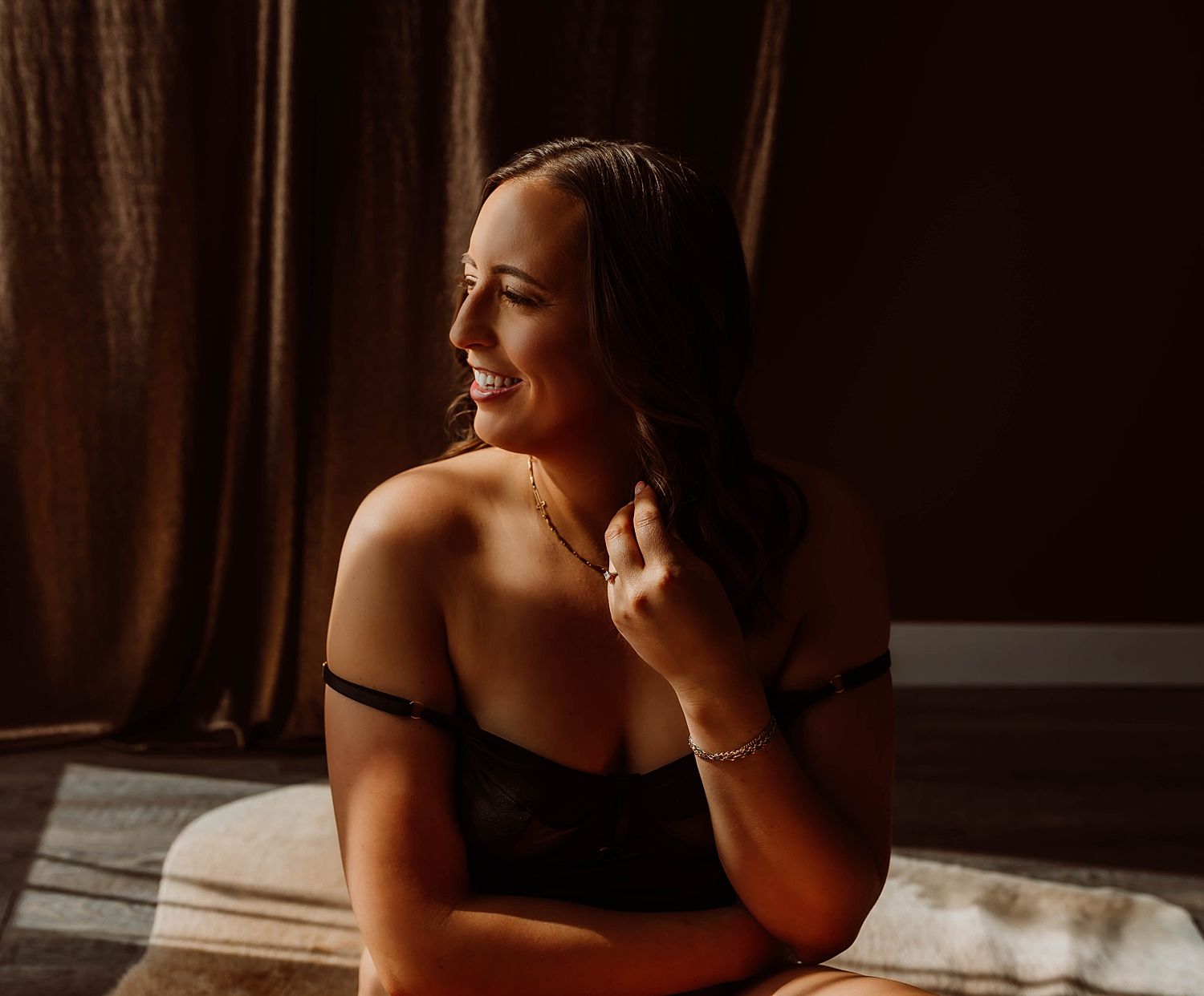 brunette in black bodysuit in front of window after learning what you need to know about boudoir